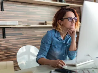 Eine Frau sitzt an einem Schreibtisch, die Hand am Kinn